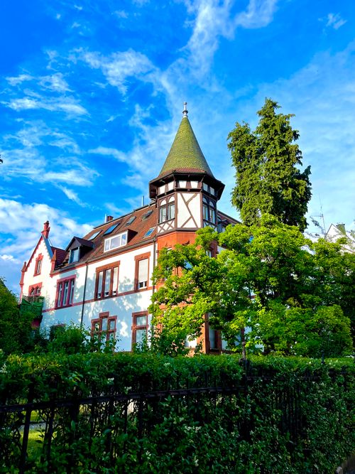 Free Beautiful historic mansion with a turret surrounded by lush greenery and vibrant blue sky. Stock Photo