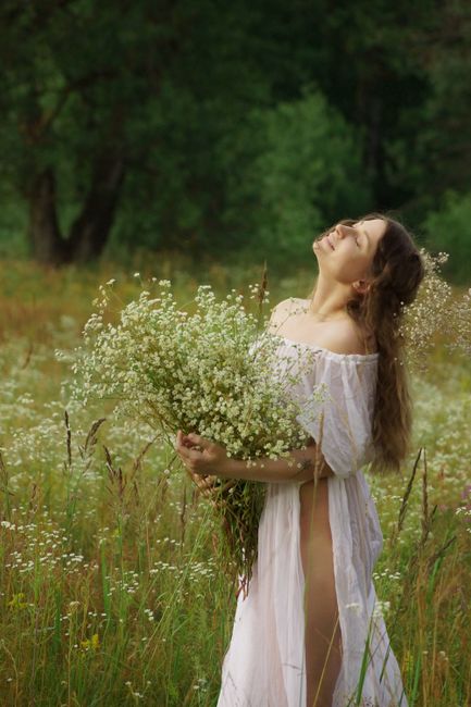 Serene woman in white dress enjoying nature, surrounded by wildflowers in a sunny meadow.