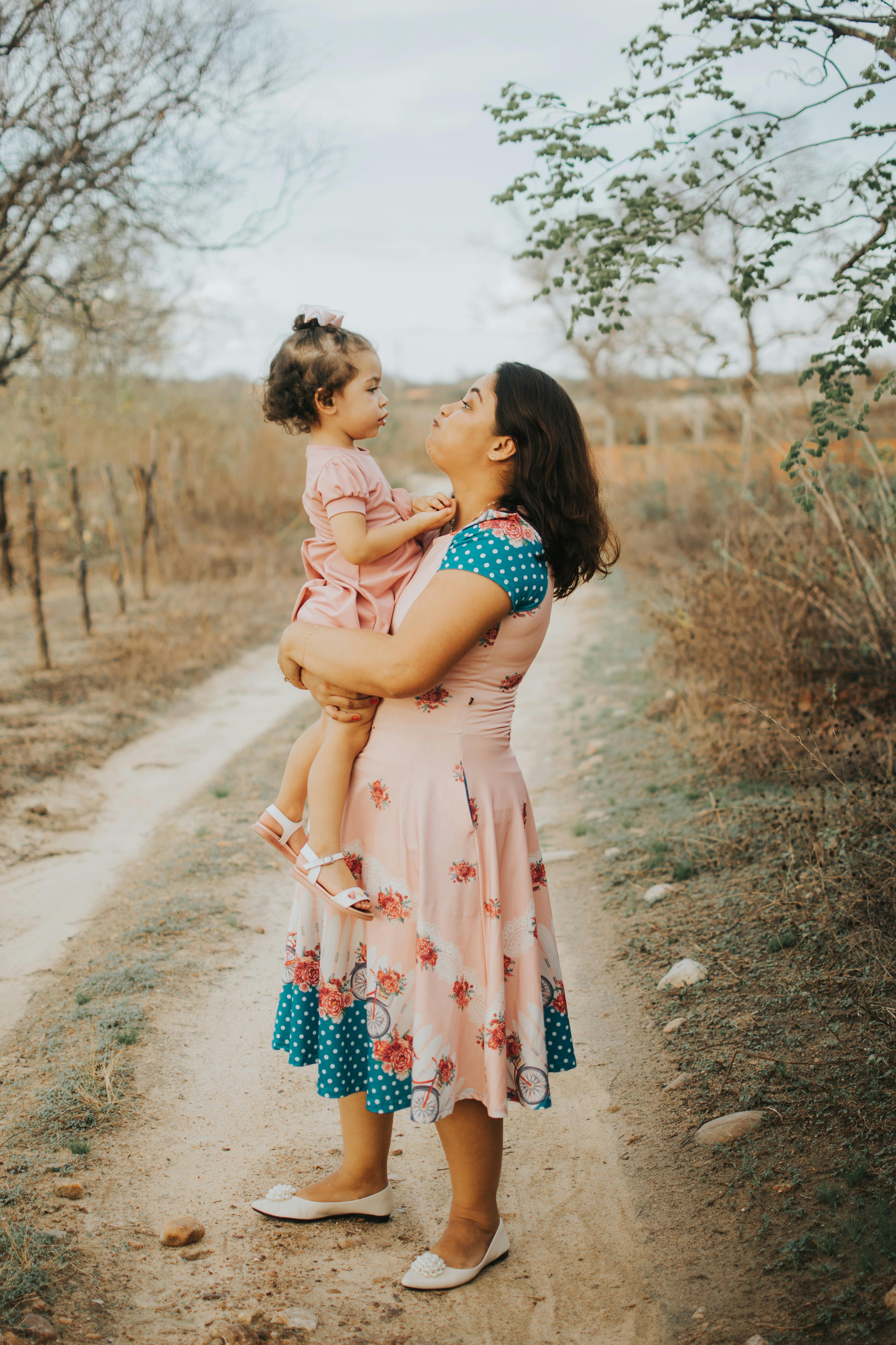 A mother holds her daughter lovingly outdoors, surrounded by nature.