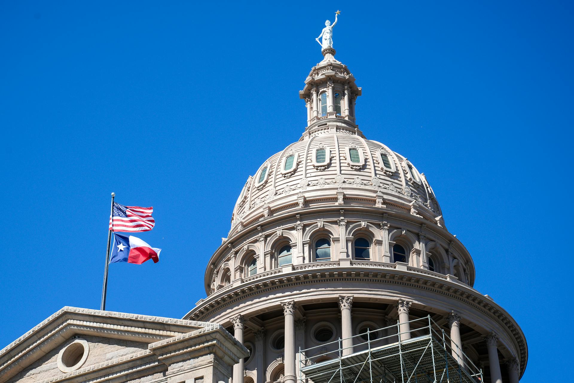 Close-up view of the Texas State Capitol dome in Austin with flags against a clear blue sky.