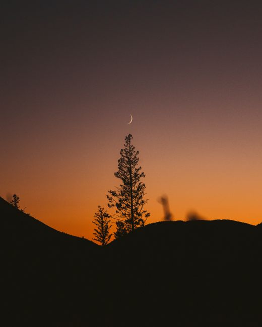 Peaceful mountain silhouette and crescent moon against a colorful sunset sky.