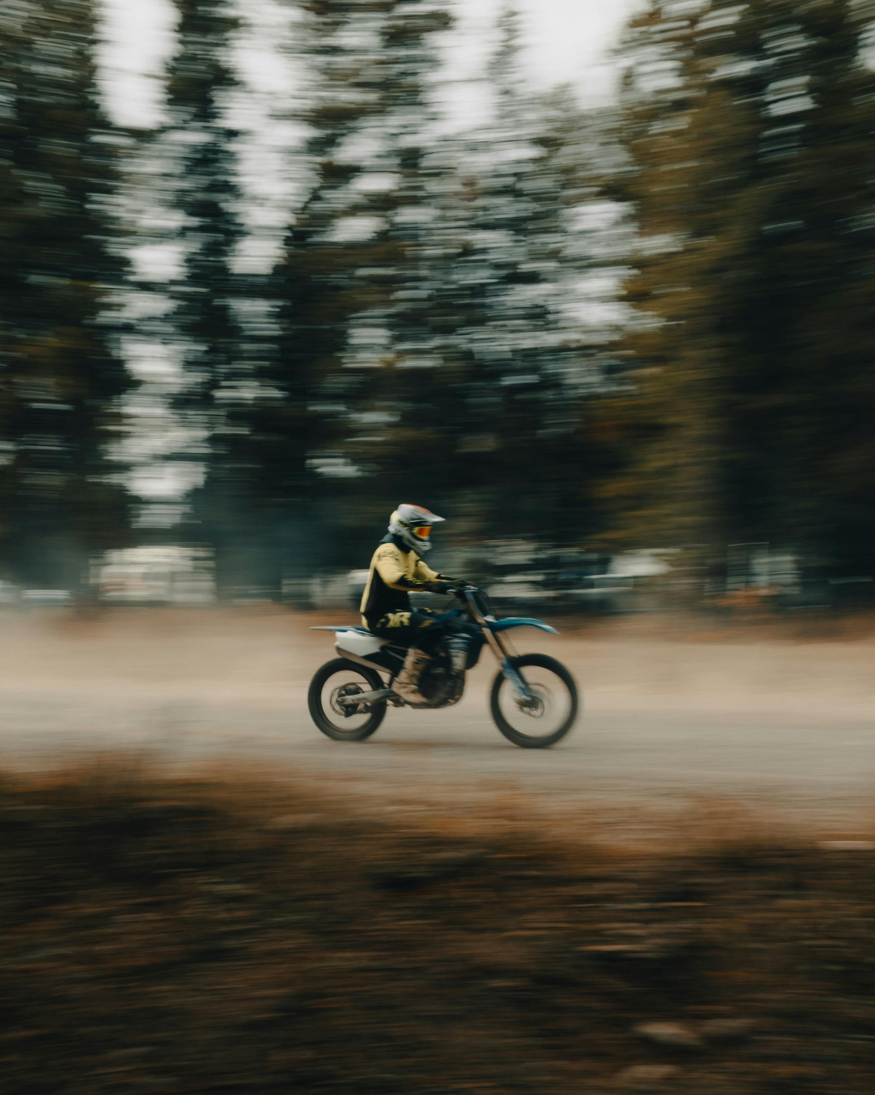 Blurred shot of a dirt bike rider speeding through a wooded area, showcasing action and excitement.