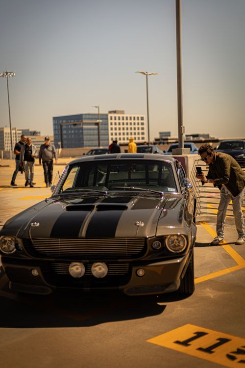 Free A classic Ford Mustang GT500 parked at an outdoor car show with a photographer capturing its details. Stock Photo