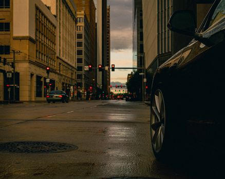 Dramatic city street view at twilight with cars and illuminated stoplights reflecting off wet pavement.
