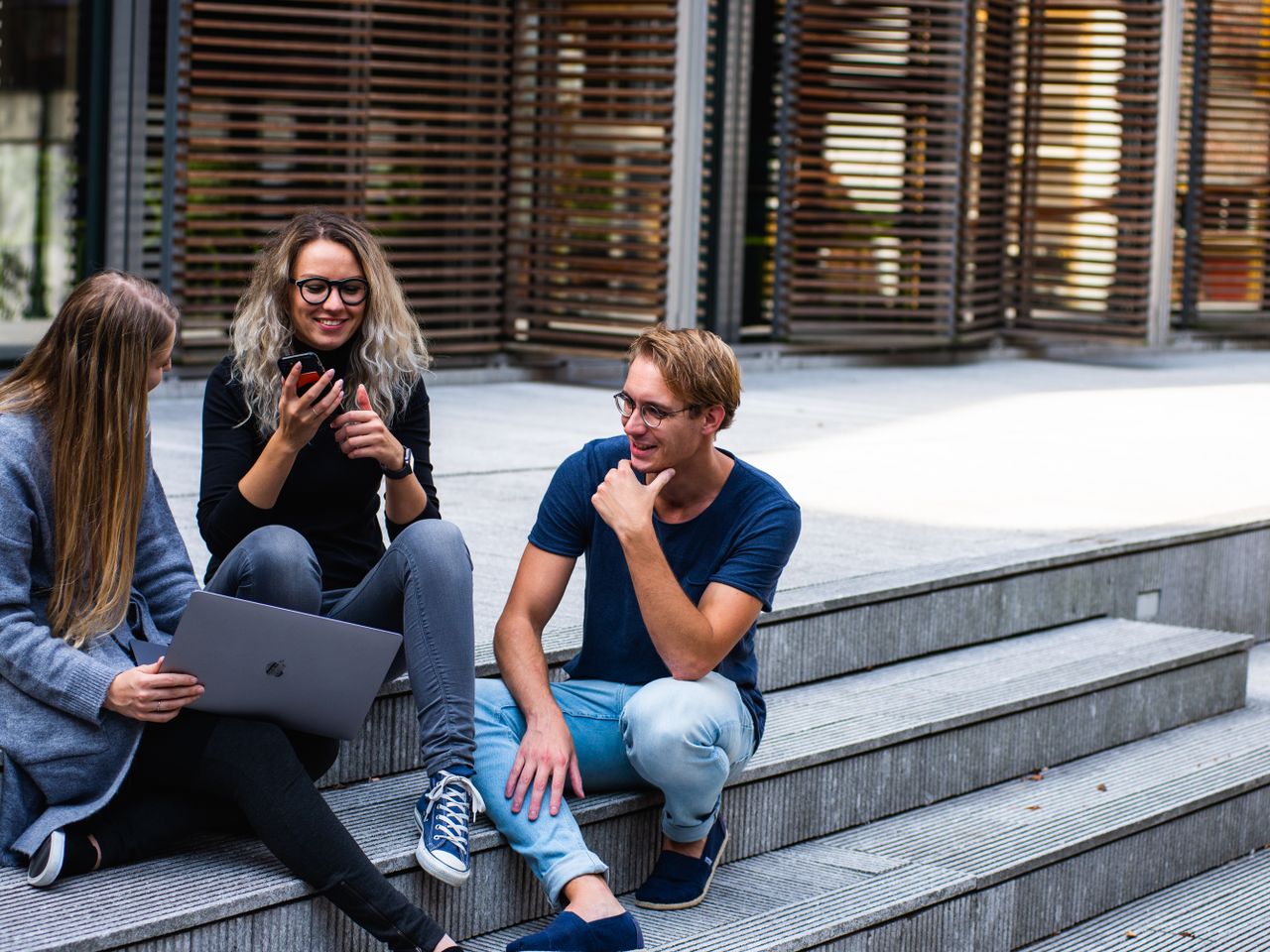 Two students collaborating on a laptop outside a modern university building