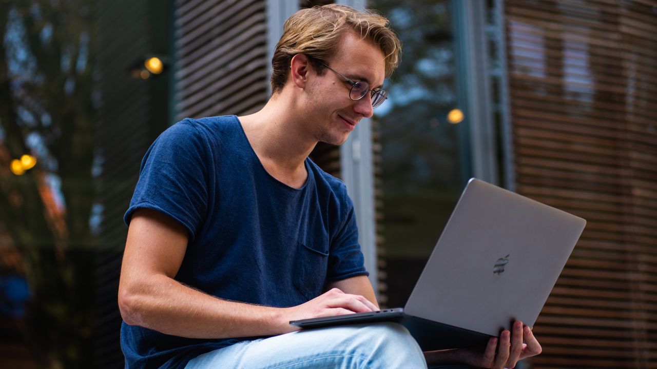 A young man sitting outdoors in Leiden, Netherlands, working on a laptop.