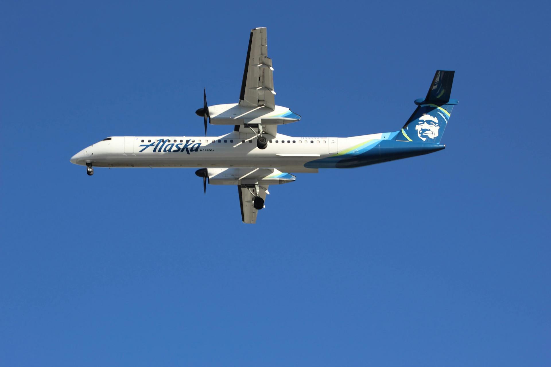 An Alaska Airlines aircraft flying against a clear blue sky in a daytime setting.