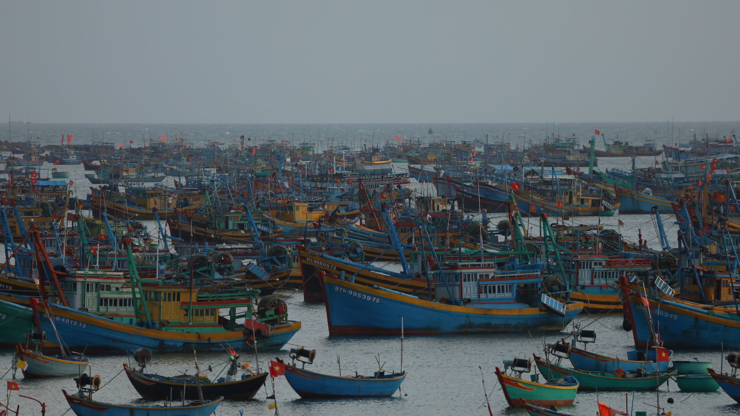 A crowded harbor scene with colorful fishing boats in Vietnam under a clear sky.