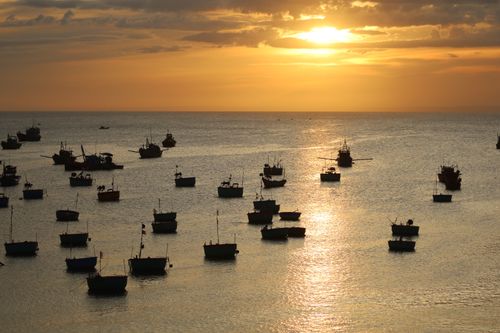 Free Silhouetted fishing boats float on the ocean during a stunning sunset, creating a serene seascape. Stock Photo