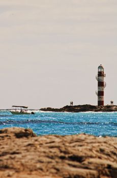 Stunning view of a lighthouse on rocky shores with a vibrant ocean backdrop in Cancún, Mexico.