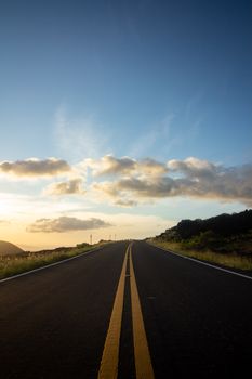 A deserted highway leading to the horizon under a vibrant golden hour sky in Hawaii, USA.