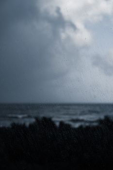 A moody scene capturing rainfall over a dark ocean with a cloudy sky, evoking a serene yet dramatic atmosphere.
