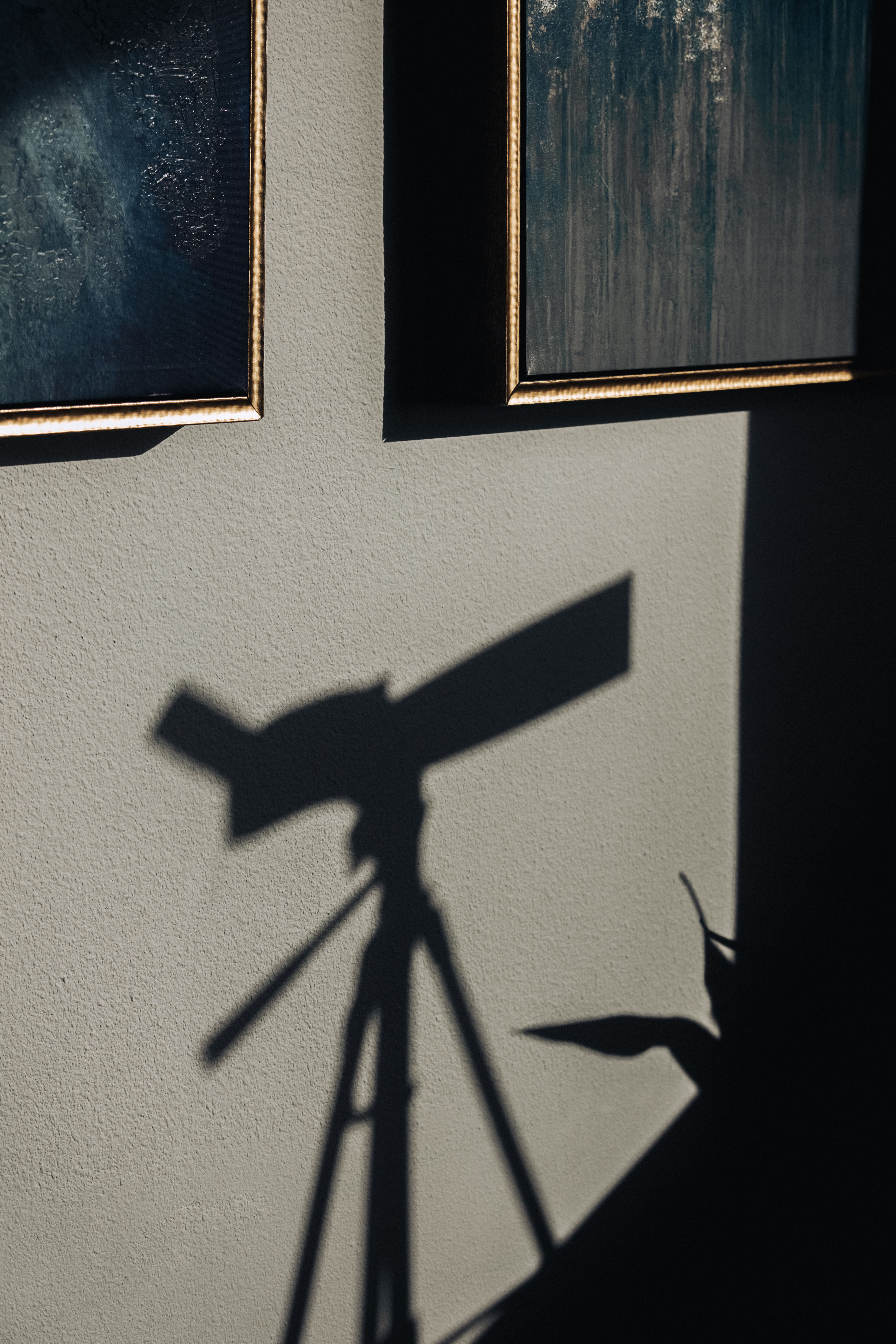 A compelling play of light and shadow with a telescope silhouette on a wall beside framed art.