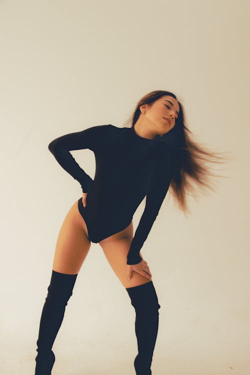 A Woman in Black Bodysuit and Boots Posing with Her Eyes Closed