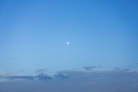 Serene view of the moon in a clear blue sky with scattered clouds, perfect for nature and tranquility themes.