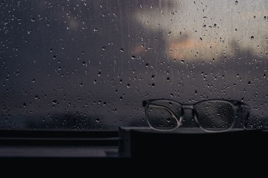 Glasses on a windowsill against a moody, rain-speckled window at twilight.