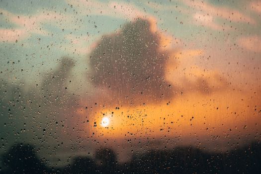 Rainy evening view through a window with sunset and clouds in the background.