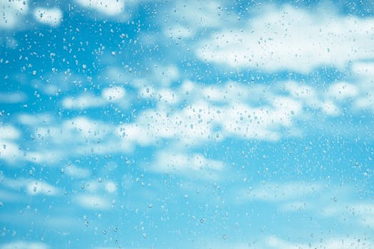 A clear view of raindrops on a window against a backdrop of a bright cloudy blue sky.