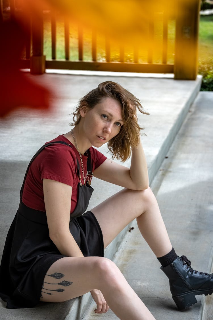 A Woman In Black Jumper Dress Sitting On A Concrete Floor