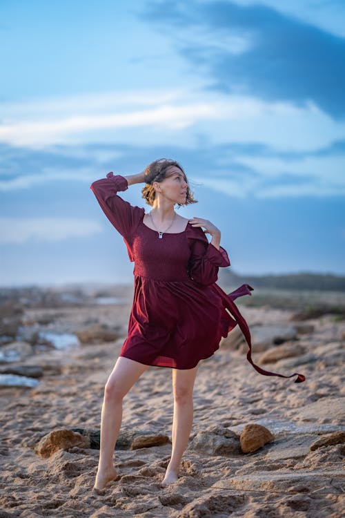 Woman in Red Dress Standing on Brown Sand