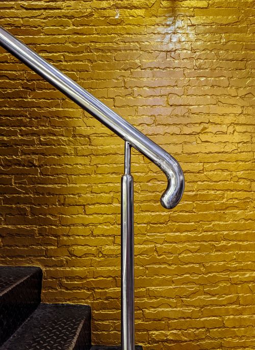 Free A modern staircase with a metallic handrail against a vibrant yellow brick wall, showcasing industrial design. Stock Photo