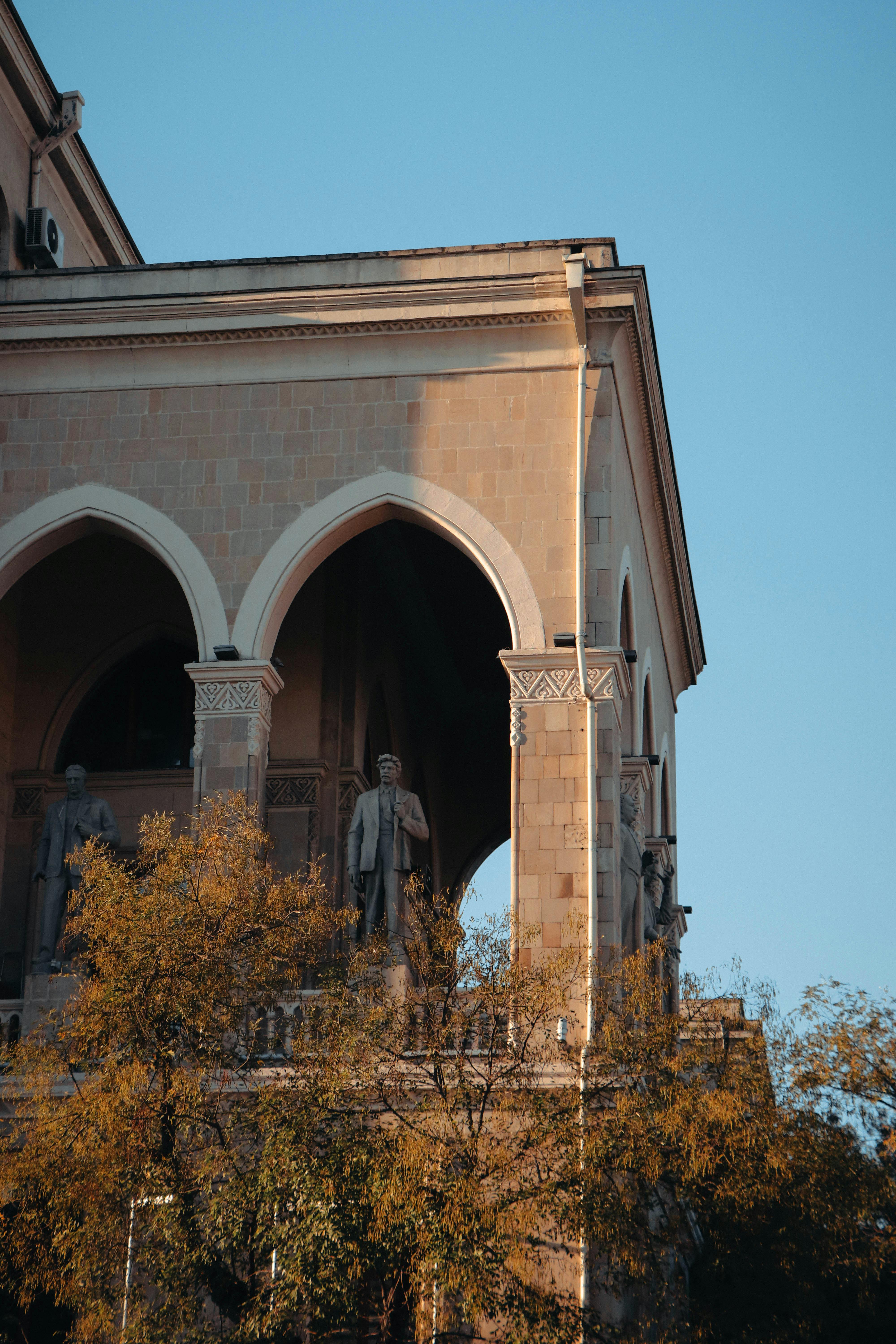 Scenic view of Mirza Fatali Akhundov Library facade with statues, arches, and autumn trees in Baku, Azerbaijan.