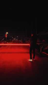 A man stands on a road illuminated by red light at night. Dramatic scene.