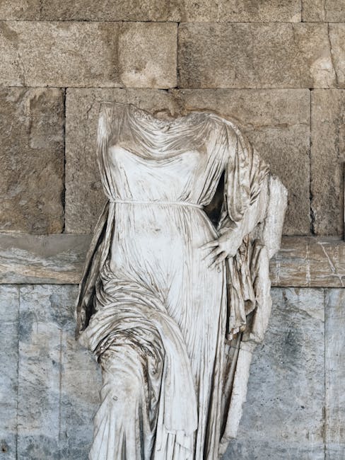 Close-up of an ancient headless marble statue draped in robes against a textured stone wall.