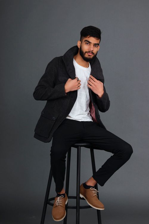 Free Stylish bearded man in black jacket sitting confidently on a stool in studio setting. Stock Photo