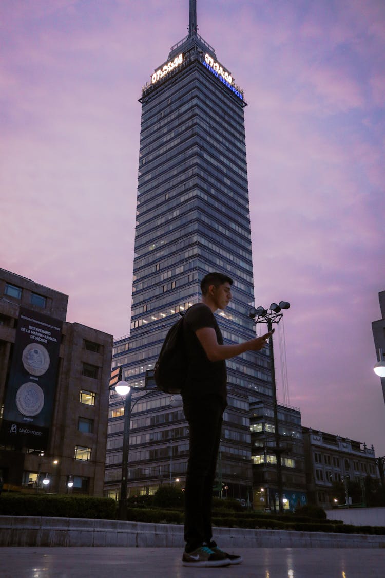 A Low Angle Shot Of A Man In Black Shirt Standing Near The Tall Building