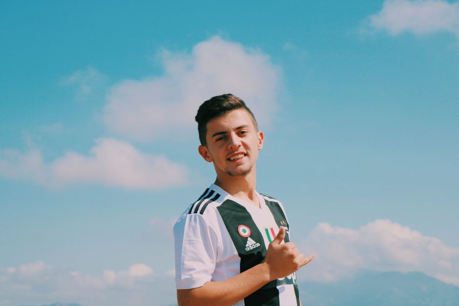 Young man smiling in a casual sports jersey under a clear summer sky.