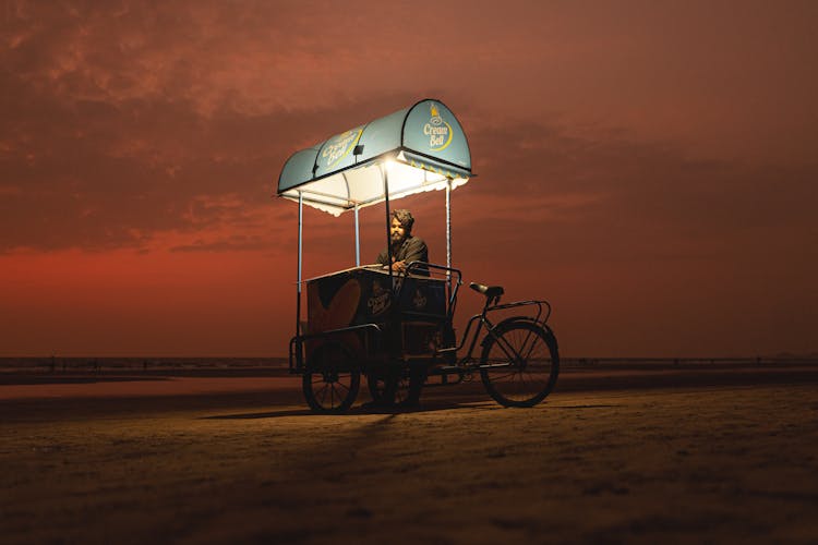 Man With An Ice Cream Trike On The Beach At Sunset 