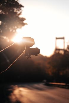 Silhouette of a hand holding a camera capturing a scenic sunset view with trees and a bridge.