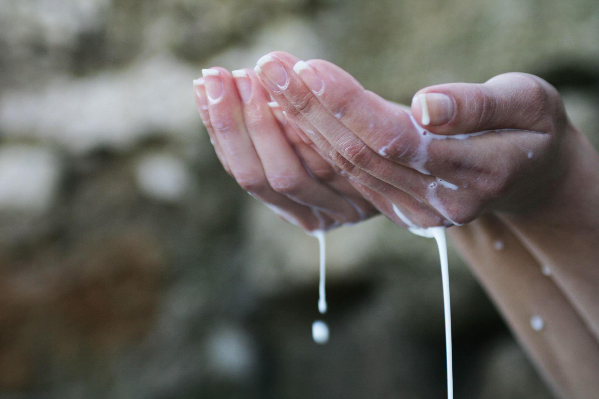 Close-up of hands with liquid dripping through fingers, symbolizing purity or ritual in an outdoor setting.