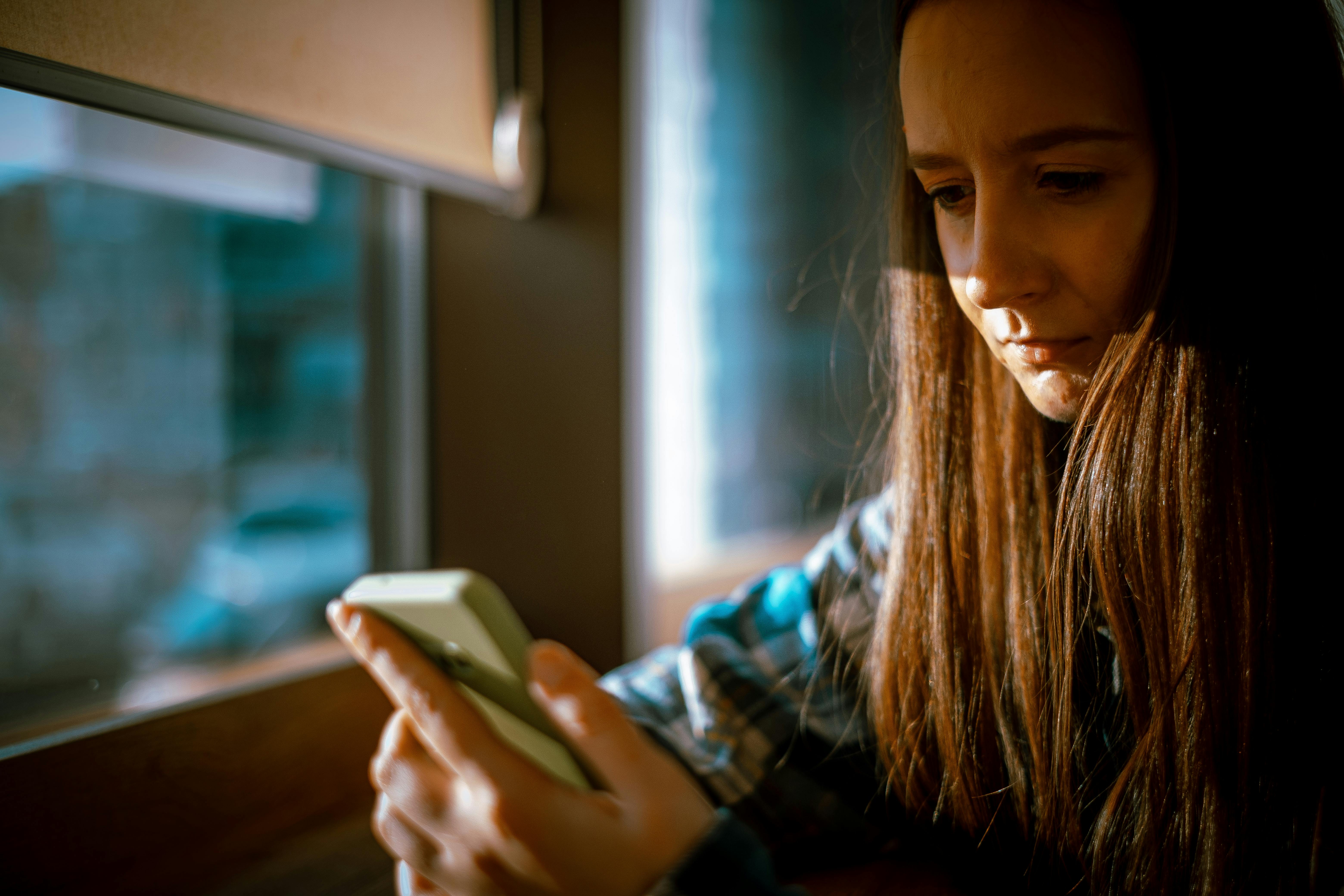Young woman looking at smartphone with sunlight streaming in through a window.