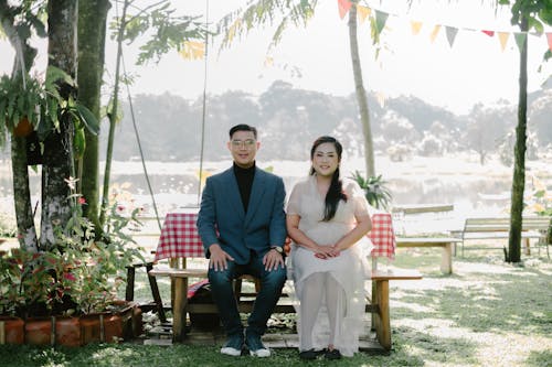 Man in Suit and Woman in White Dress Sitting on Bench at Park