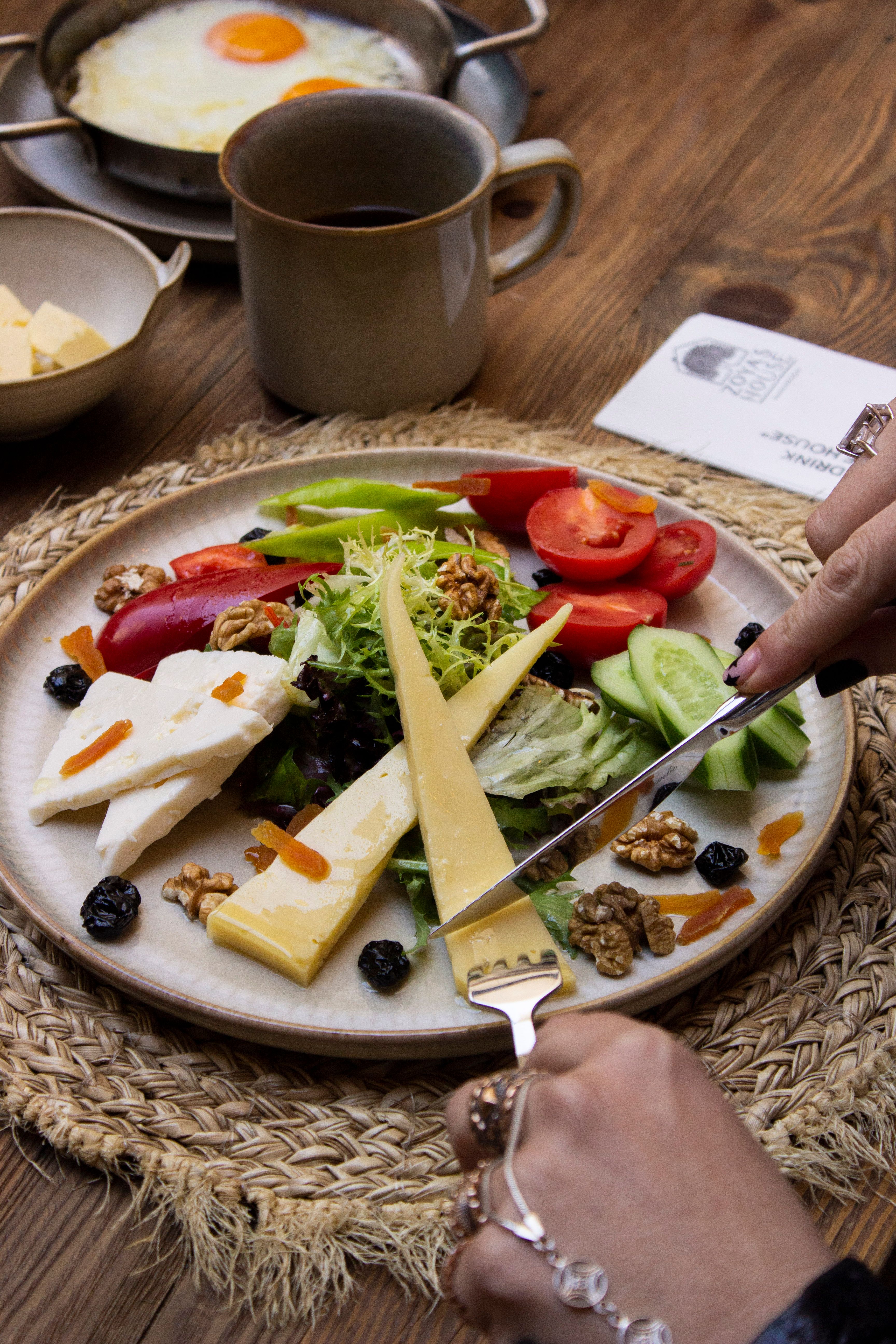 A vibrant breakfast plate featuring cheese, fresh vegetables, nuts, and a cup of coffee.