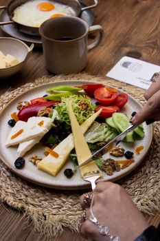A vibrant breakfast plate featuring cheese, fresh vegetables, nuts, and a cup of coffee.