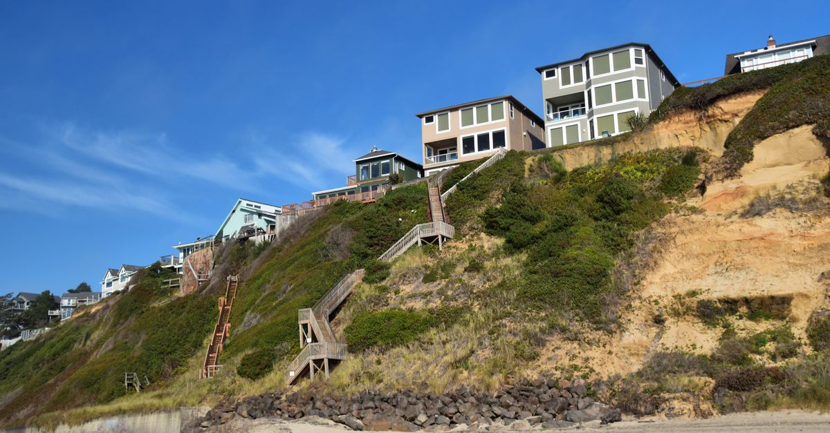 Stunning cliffside houses overlooking a sandy beach on a clear day with blue skies.