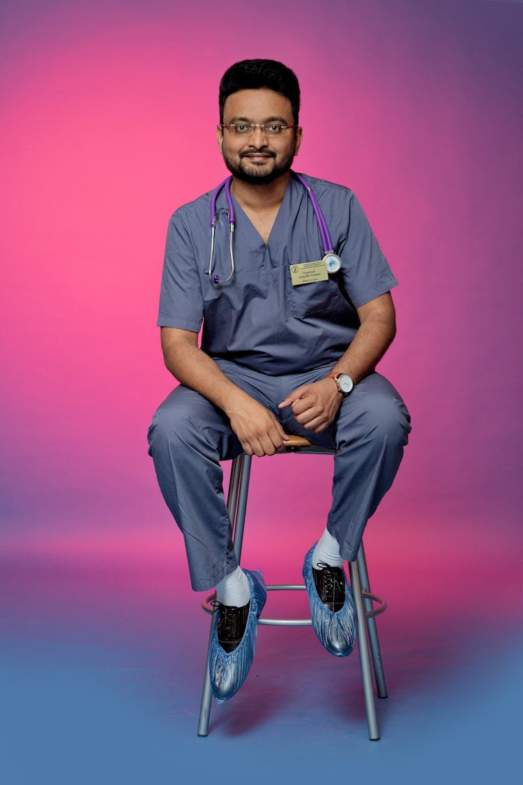 A Man In Medical Scrubs Sitting On The Stool