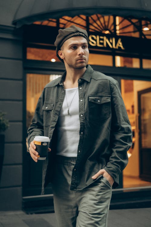 A Man in Black Jacket Holding a Cup of Coffee while Walking on the Street