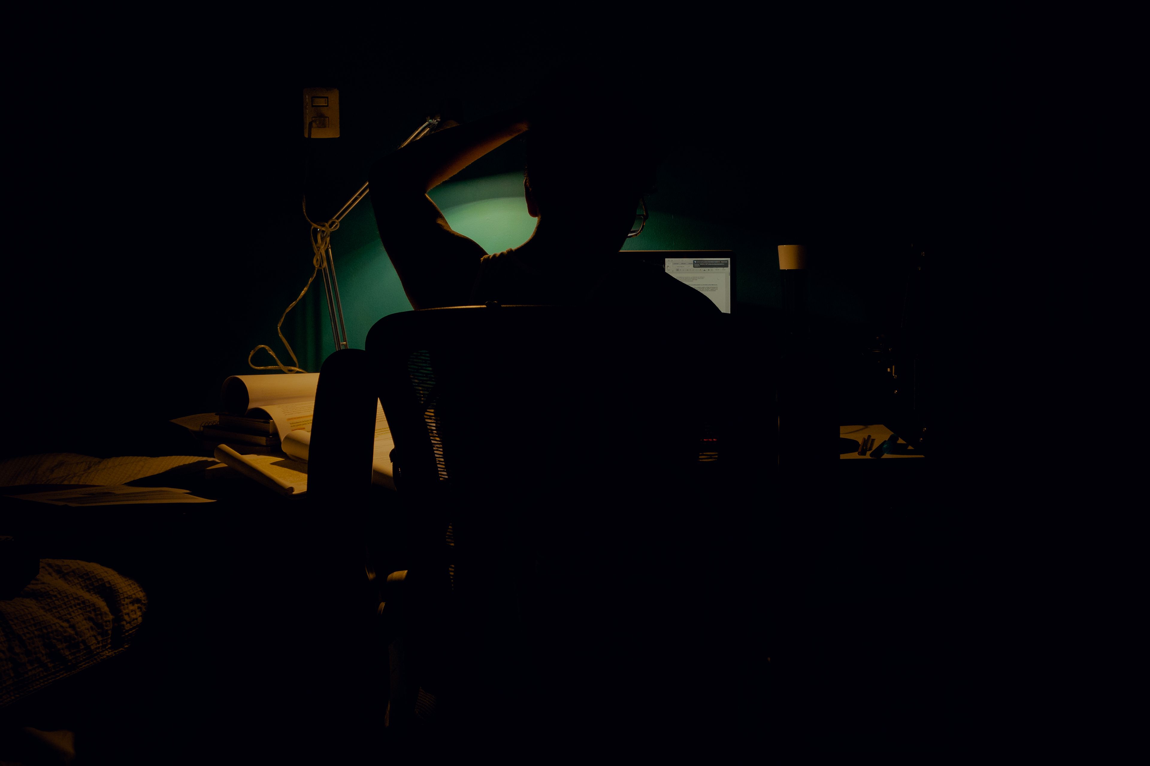 A person's silhouette illuminated only by the glow of a computer screen in a dark room — a fitting metaphor for the quiet, solitary relationship many ADHD users develop with AI tools.