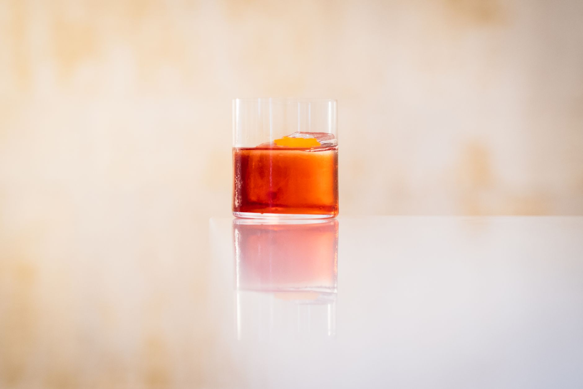 A single amber cocktail in a tumbler on a pale surface