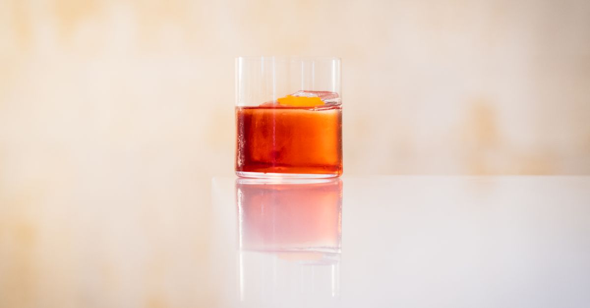 Elegant glass of Negroni with orange peel garnish on reflective surface, perfect for lifestyle and drink concepts.