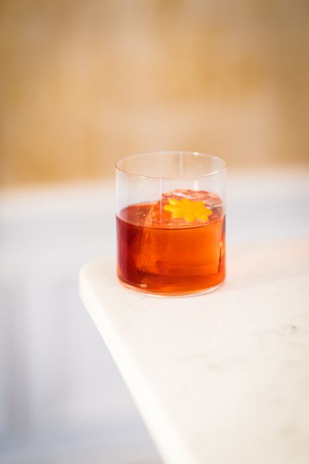 A ruby-red Negroni in a rocks glass over a single large ice cube, garnished with a curled orange peel, condensation beading on the glass.