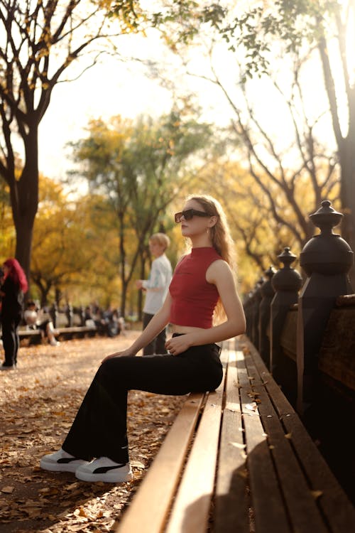 A Woman in Red Turtleneck Tank Top Sitting on a Wooden Bench