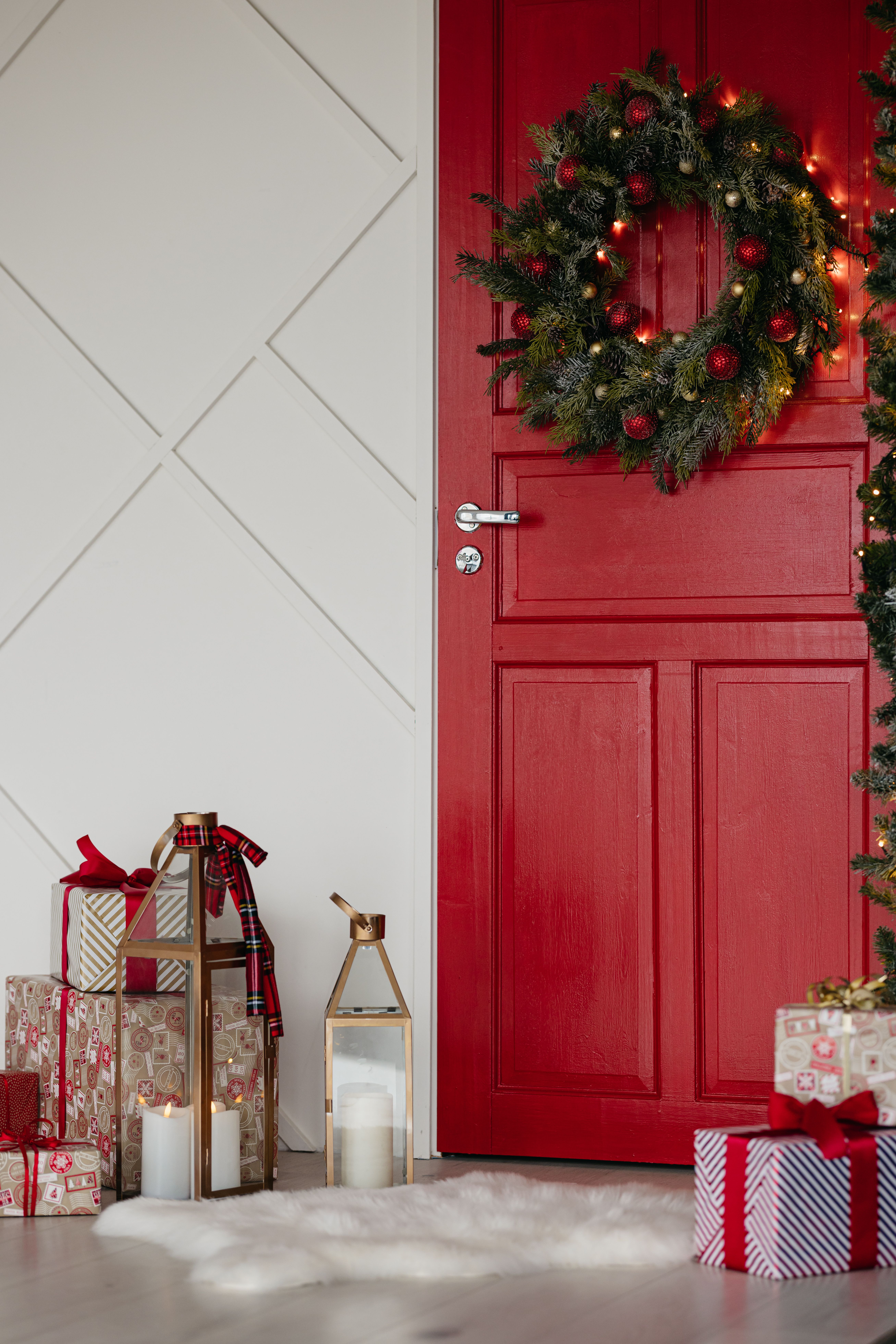 Cozy Christmas scene with wreath on red door, gifts, and candles.