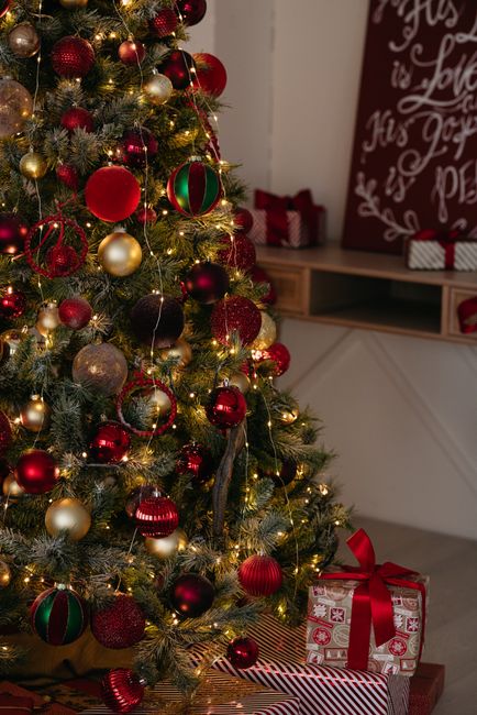 A beautifully decorated Christmas tree with ornaments and gifts set in a cozy indoor setting.