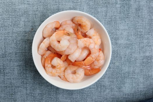 A white bowl filled with fresh cooked shrimps on a textured surface.