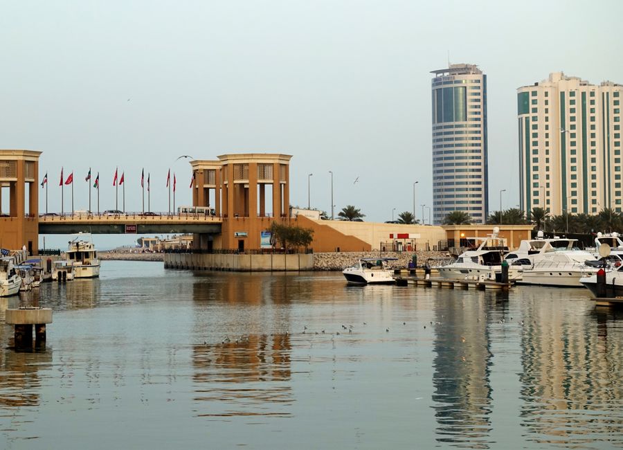 A modern marina with yachts, bridge, and waterfront city skyline reflecting on calm waters.